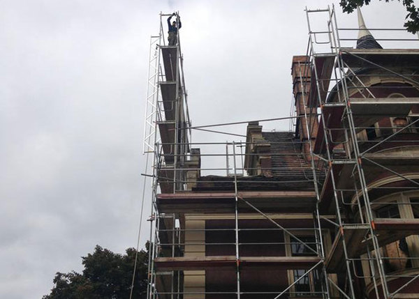 Gerüstbau an historischem Gebäude mit Arbeiter auf hohem, schmalem Baugerüst bei Renovierung.