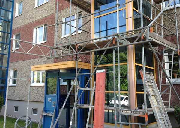 Mehrfamilienhaus mit Baugerüst am Eingang, Aufzugmodernisierung und Fassadensanierung.