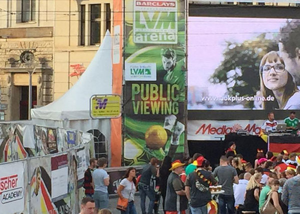 Menschenmenge beim Public Viewing eines Fußballspiels auf großer Outdoor-Leinwand.