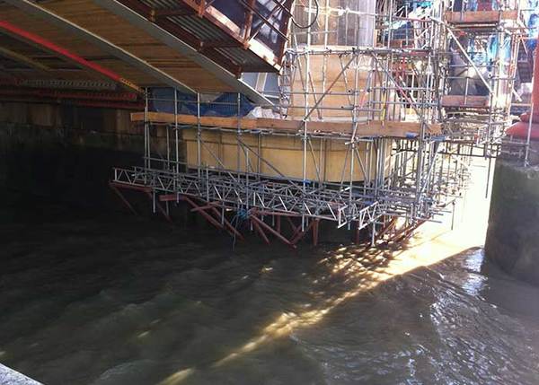 Baugerüst unter Brücke an Flussufer für Brückenbauarbeiten und Instandhaltung.