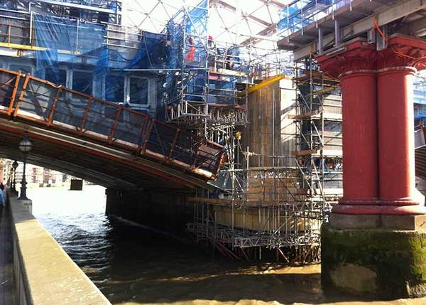Brückenbauarbeiten mit Gerüsten und Stahlträgern über einem Fluss bei Tageslicht.